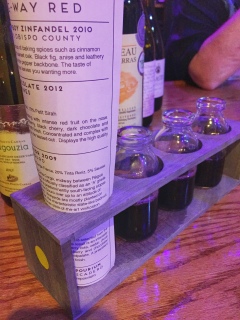 Small wooden rack with mini jugs containing the wine flight served.